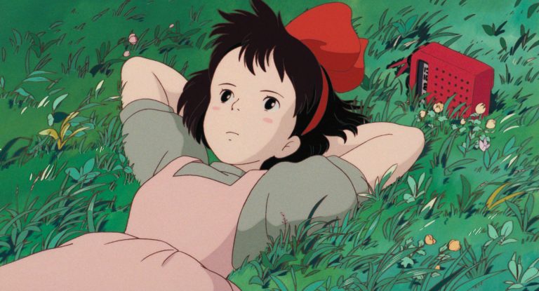 Kiki resting in grass beside her red radio