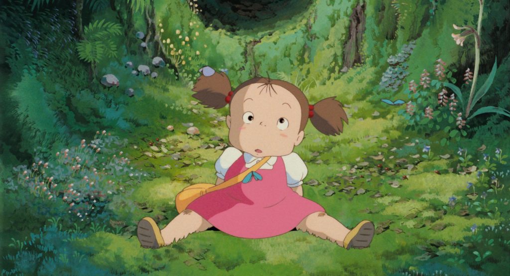 Mei sitting alone on a forest path surrounded by summer plants